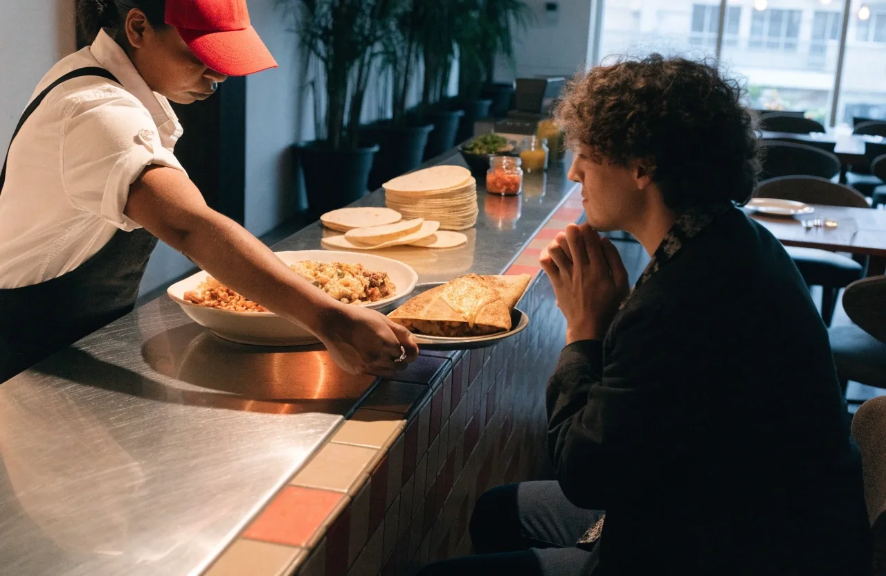Staff building a burrito bowl at the counter in front of a guest
